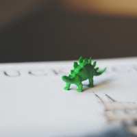 a green toy dinosaur is sitting on top of a book
